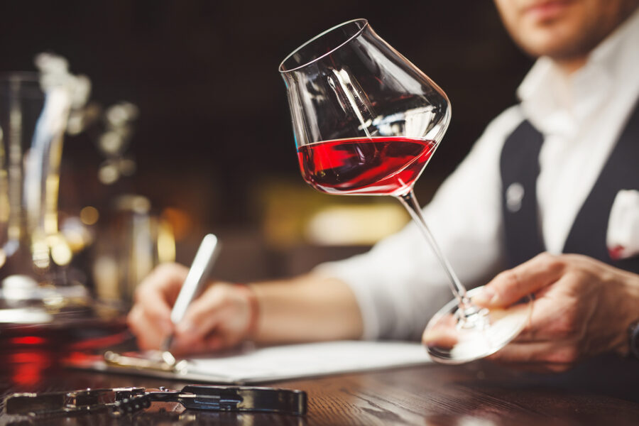 Sommelier fills form describing quality of expensive red wine in wineglass sitting at table in luxury restaurant closeup
